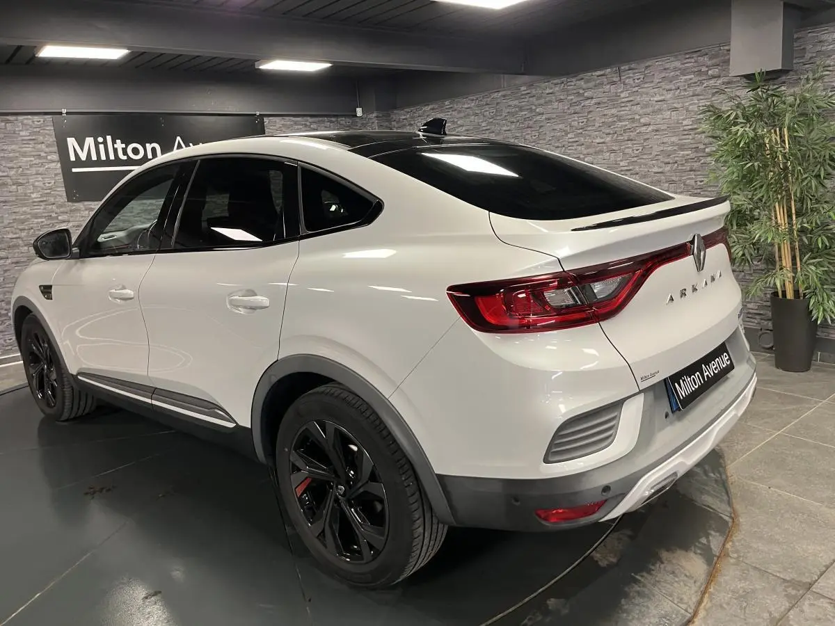 Vue 3/4 arrière droite d'une Renault Arkana blanche avec toit noir brillant et jantes noires R.S. Line dans un showroom.