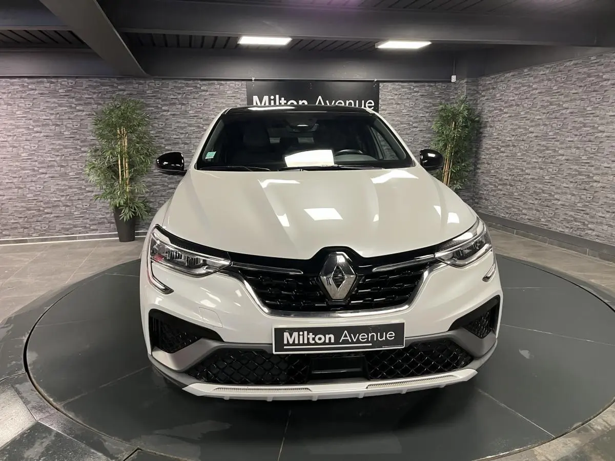 Vue frontale d'un Renault Arkana blanc perle avec calandre noire et logo Renault au centre, en showroom.