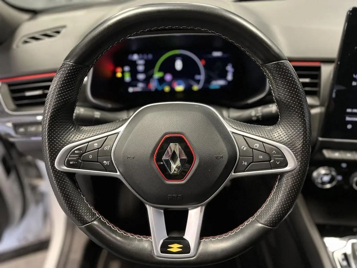 Volant sport en cuir noir avec surpiqûres rouges et logo Renault au centre, tableau de bord numérique en arrière-plan