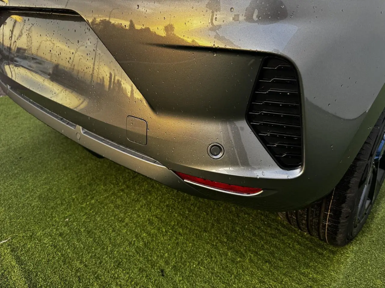 Gros plan sur le pare-chocs arrière droit gris schiste métallisé de la Renault Clio V avec capteur de stationnement et feu rouge.