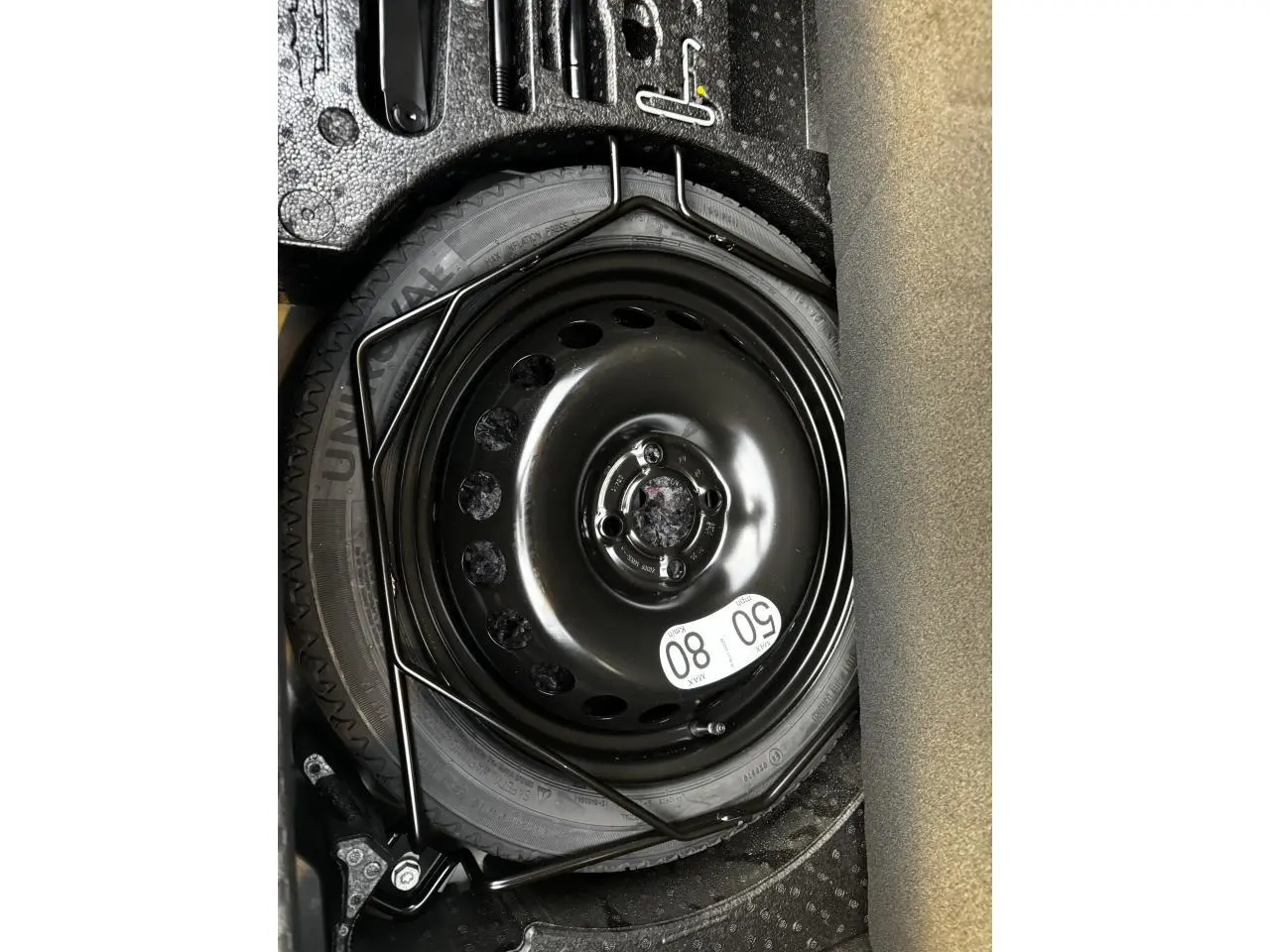 Roue de secours noire avec étiquette de limitation 80 km/h dans le coffre d'une Renault Clio gris schiste.