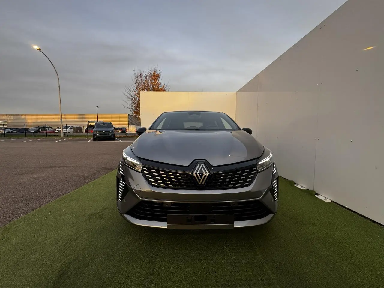 Vue de face d'une Renault Clio gris schiste métal avec calandre noire et feux LED verticaux allumés.