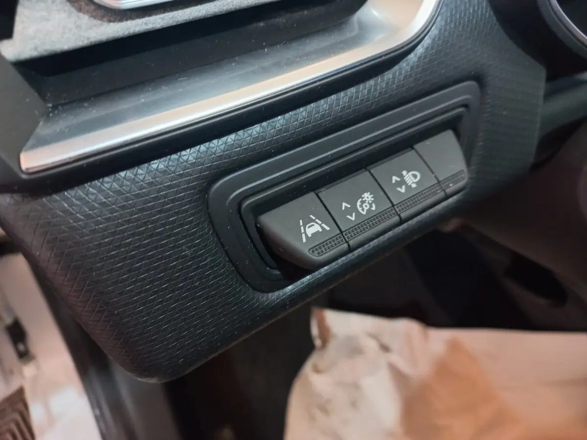 Gros plan sur les boutons de réglage d'assistance à la conduite dans l'habitacle noir de la Renault Clio Business blanche.