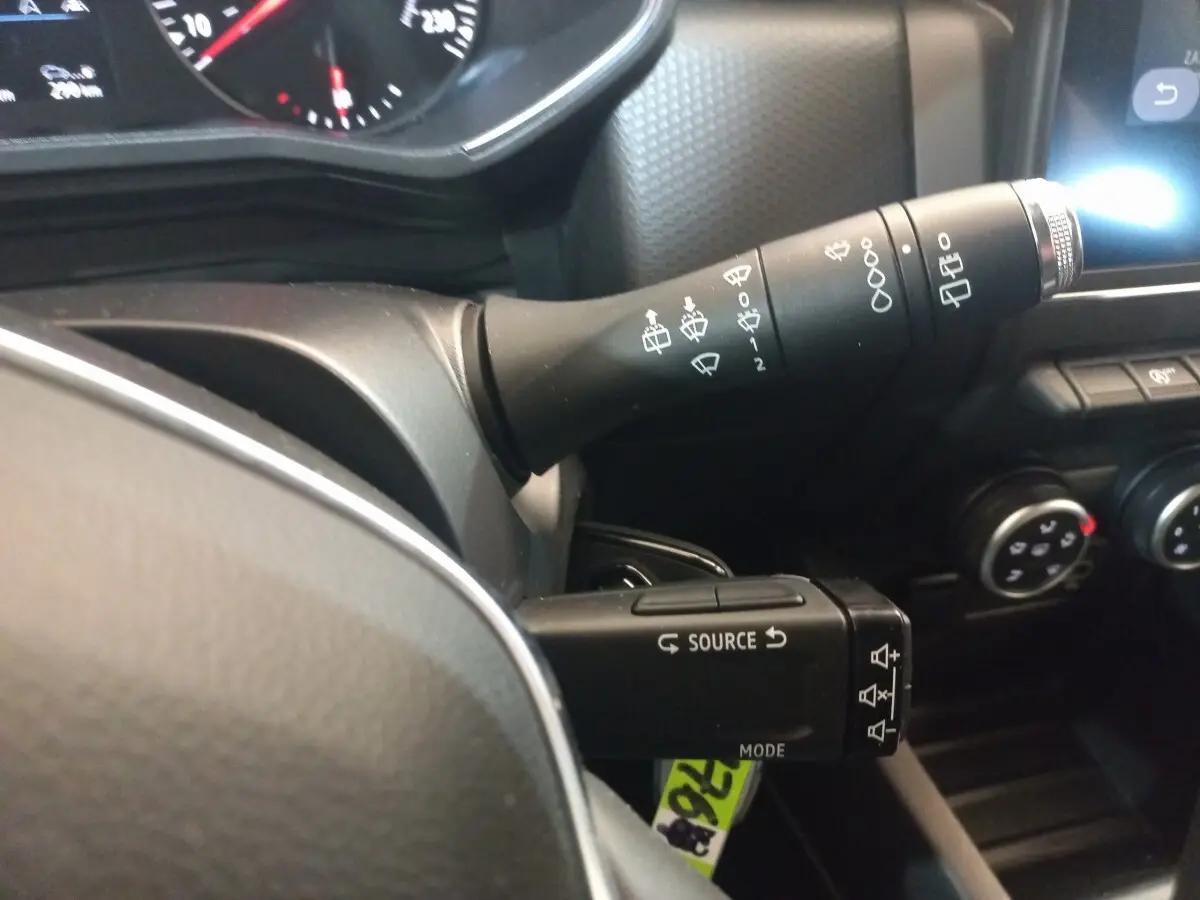 Gros plan sur les commandes au volant noir de la Renault Clio Business blanche, avec tableau de bord et boutons de climatisation visibles.