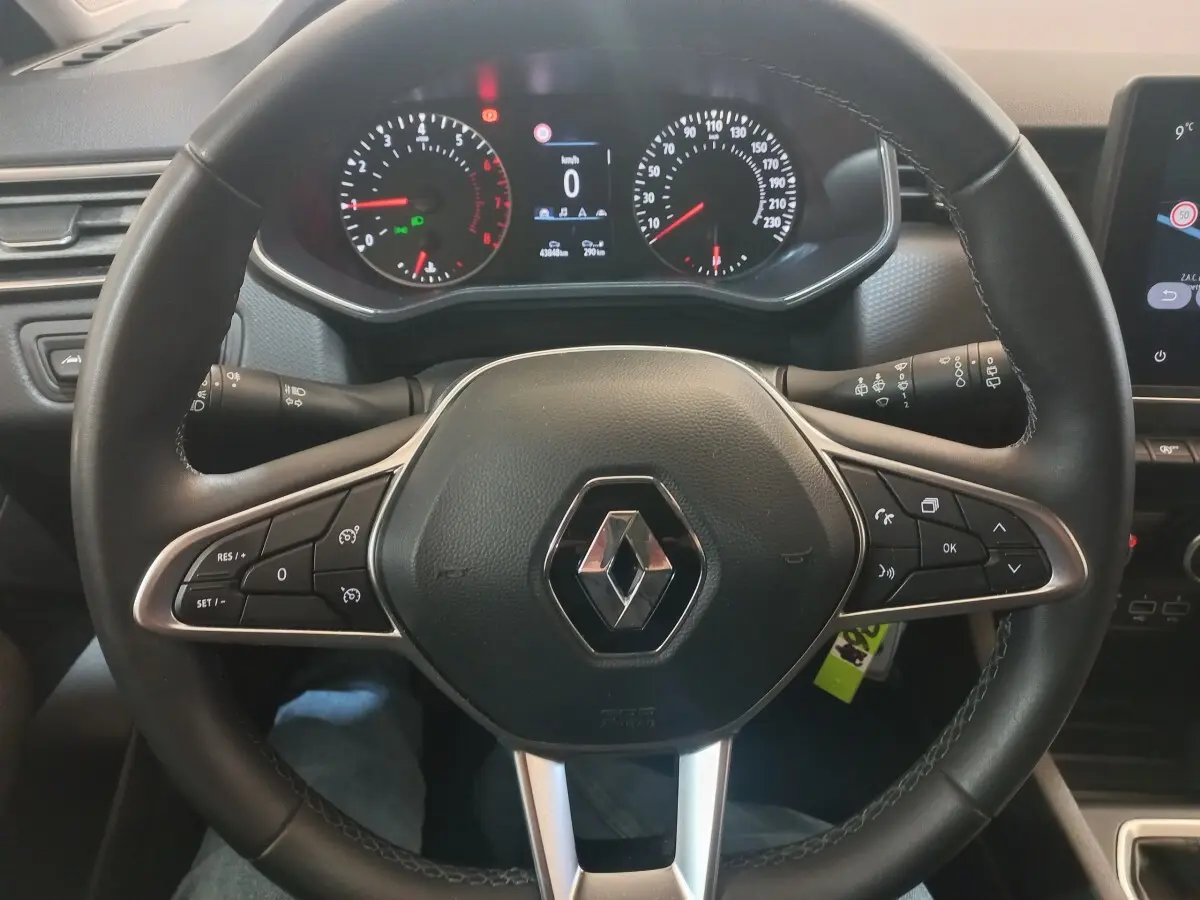 Vue rapprochée du volant en cuir synthétique noir d'une Renault Clio Business blanche, avec commandes multifonctions et tableau de bord numérique.