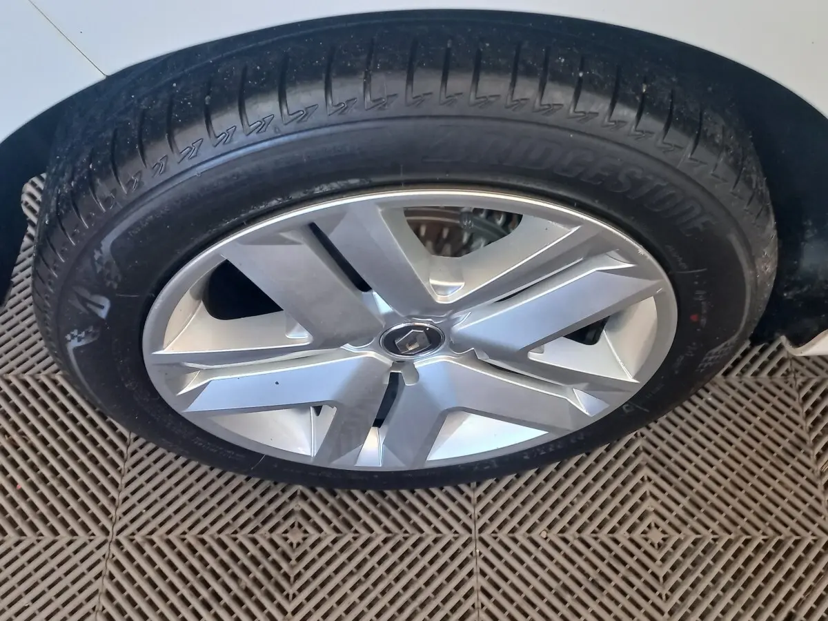 Gros plan sur la roue avant droite d’une Renault Clio blanche 2021 avec jante alliage argentée et logo Renault central.