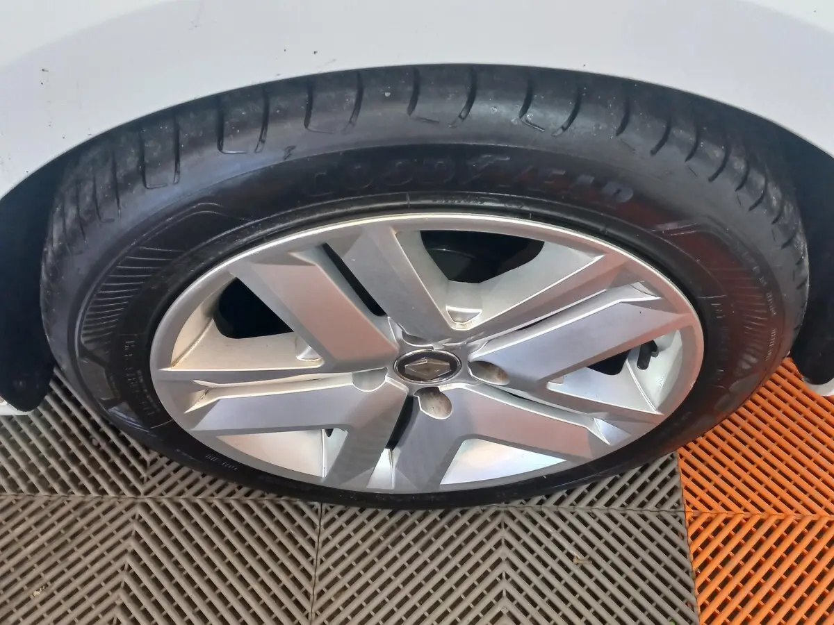 Gros plan sur la roue avant droite d'une Renault Clio blanche, jante alliage à cinq branches doubles.