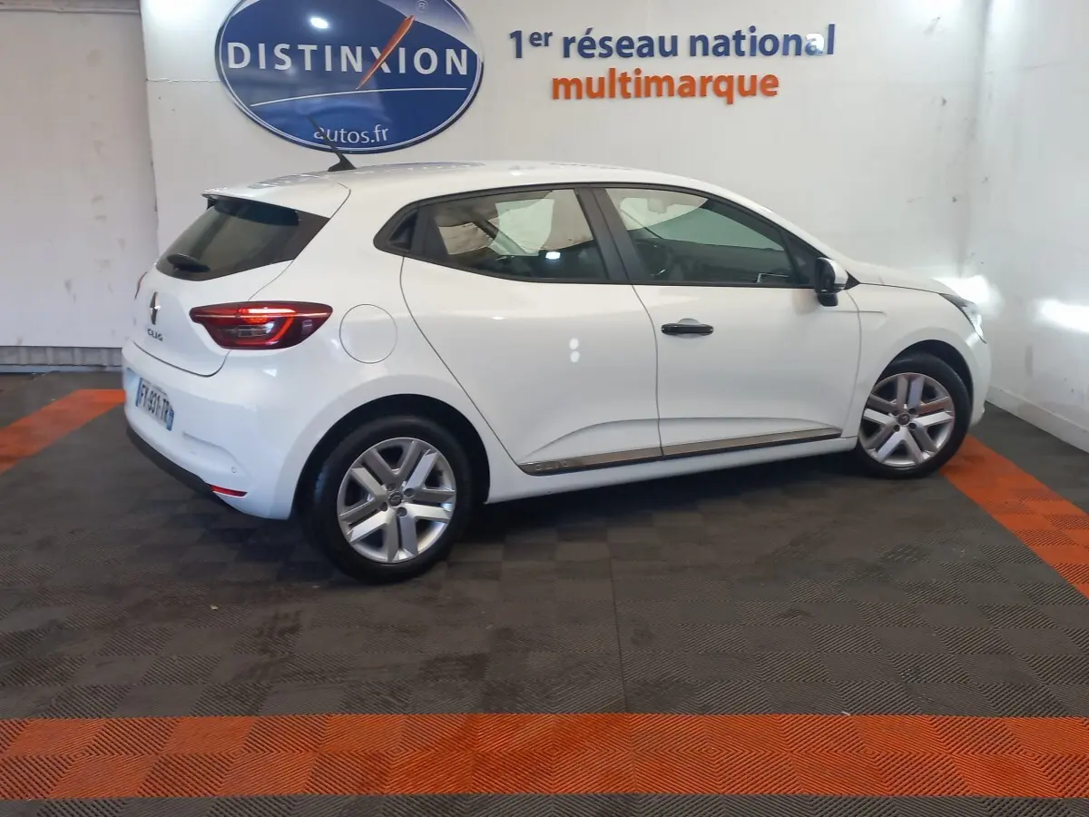 Renault Clio Business blanche vue de profil côté droit dans un showroom avec sol noir et bandes orange.