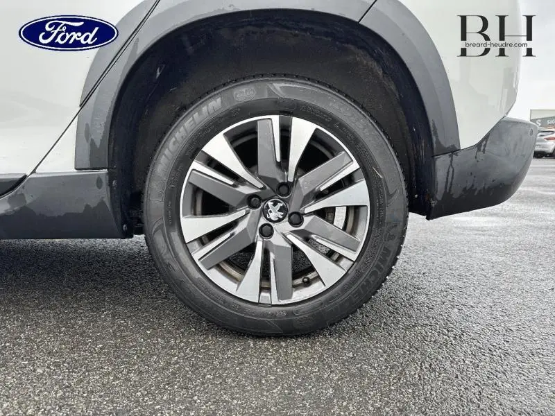 Gros plan sur la roue avant droite d'un Peugeot 2008 blanc Banquise, avec jante alu et logo lion au centre.