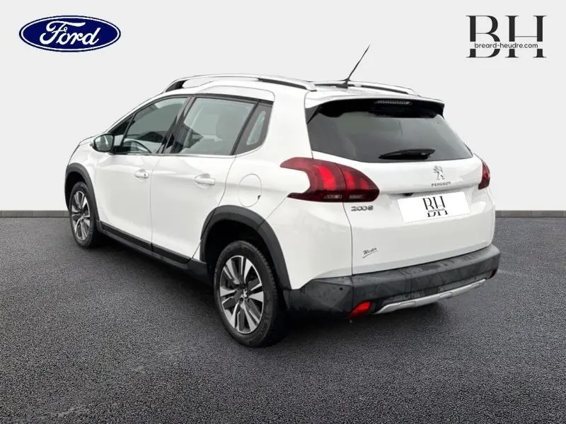 Vue 3/4 arrière droite d'un Peugeot 2008 blanc Banquise avec barres de toit et jantes alu visibles.