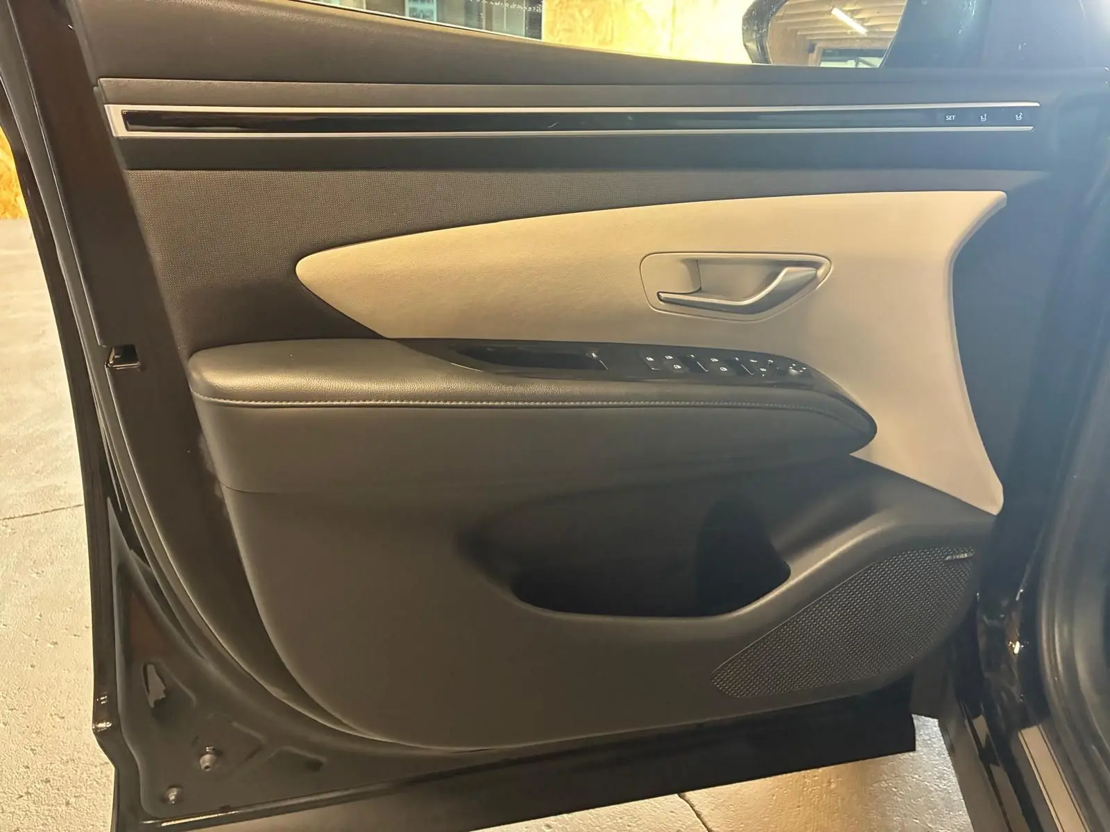 Vue rapprochée de la porte avant gauche du Hyundai Tucson noir 2022, avec garniture bicolore beige et noire et commandes électriques.