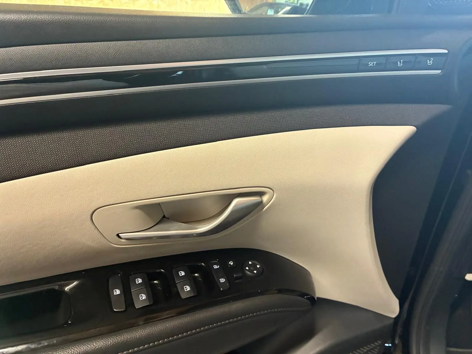 Détail de la porte avant gauche du Hyundai Tucson noir 2022, avec commandes électriques et garniture beige et noire.