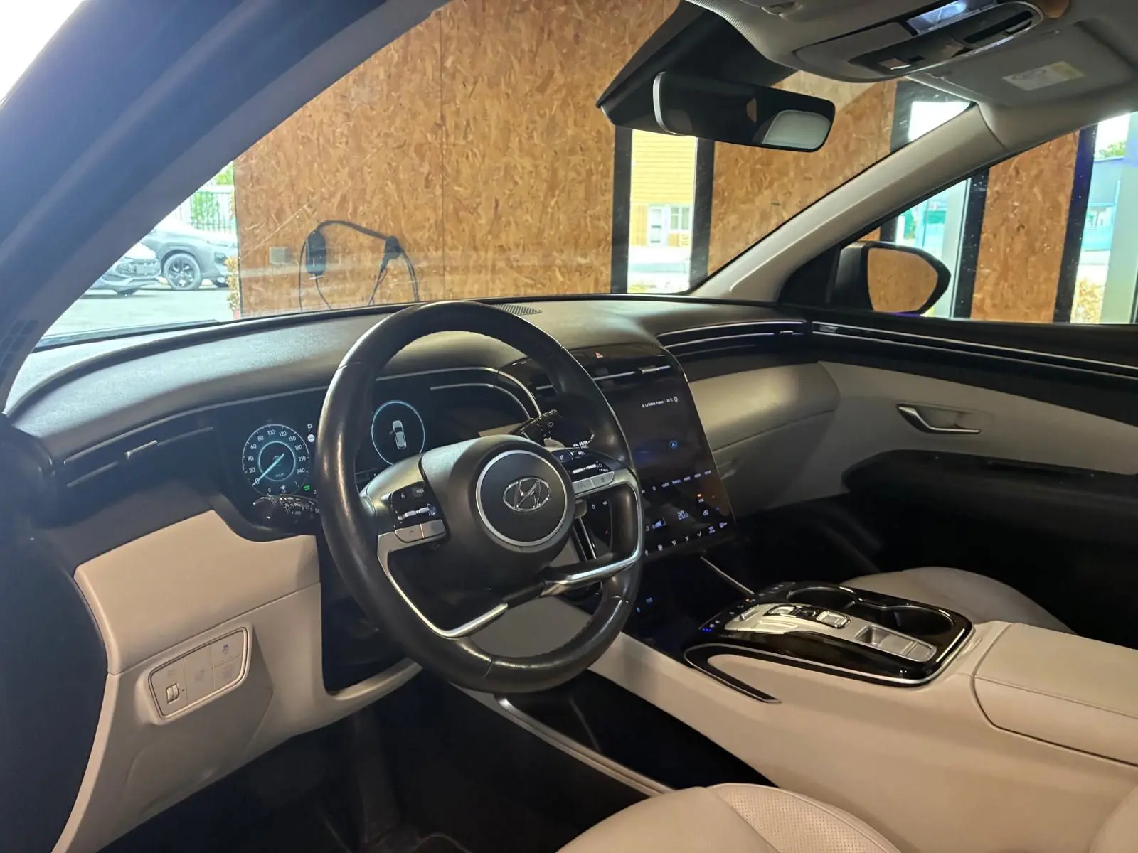 Vue intérieure côté conducteur du Hyundai Tucson 2022 hybride, avec tableau de bord numérique et sellerie beige.