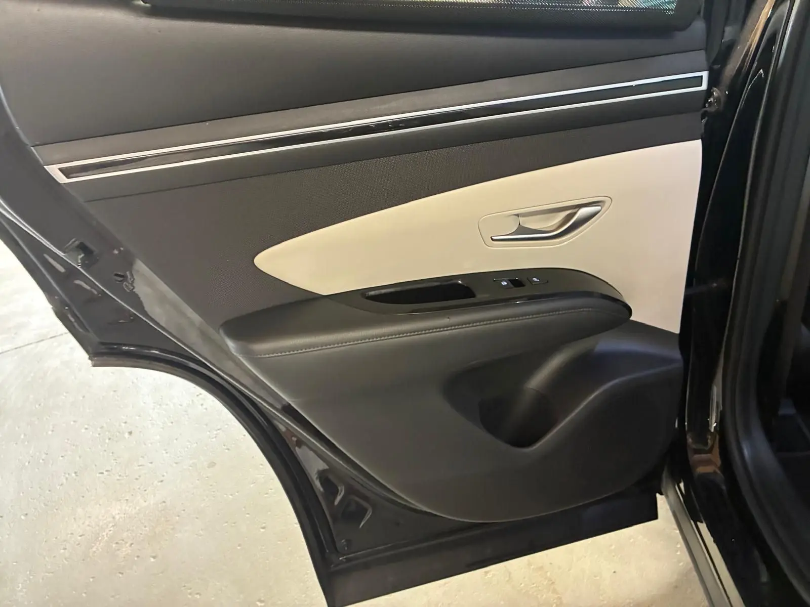 Vue rapprochée de la porte arrière gauche noire du Hyundai Tucson 2022 avec garniture intérieure bicolore beige et noire.