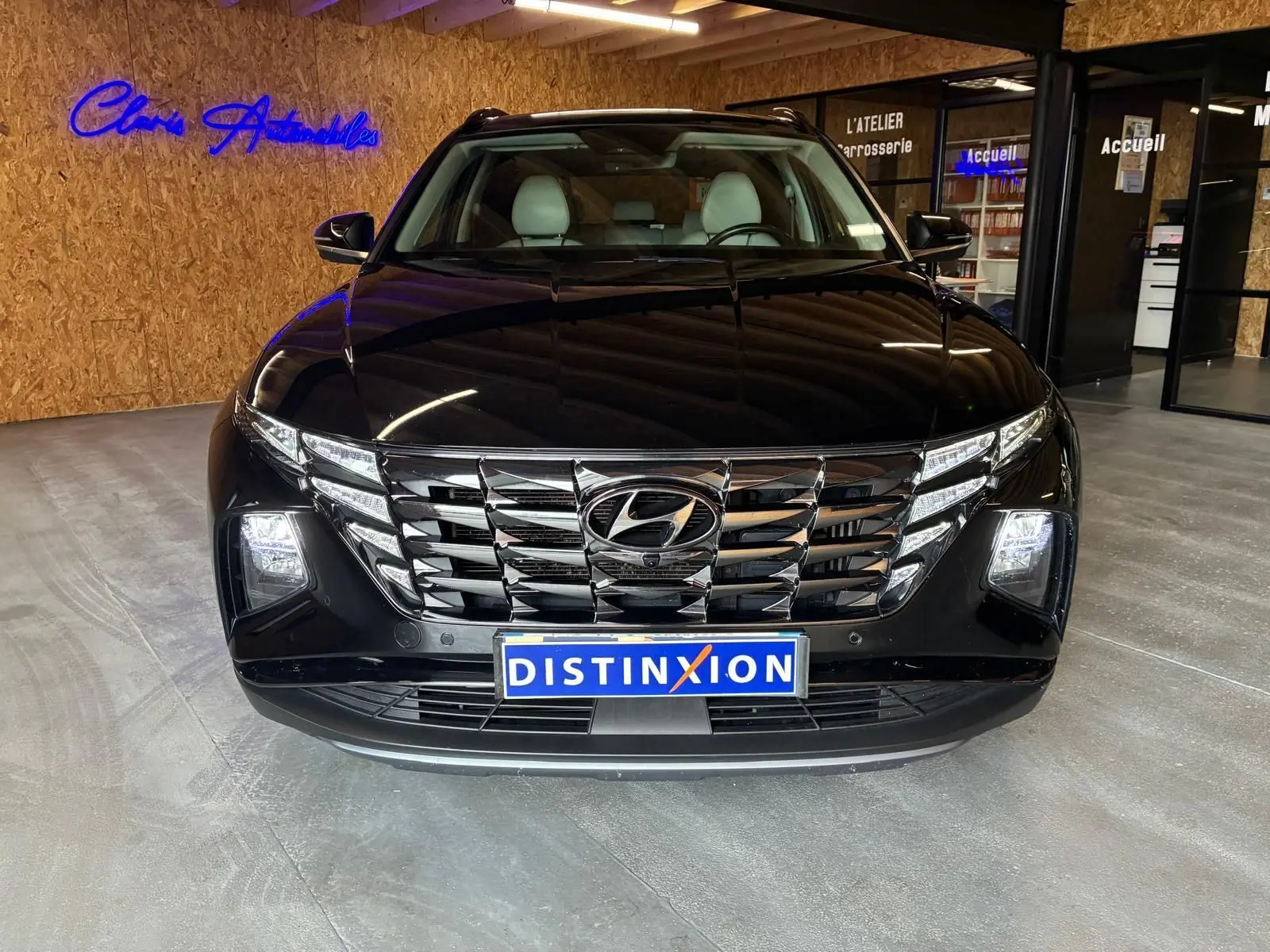 Vue avant d’un Hyundai Tucson noir 2022 avec calandre chromée et phares LED allumés en intérieur showroom.