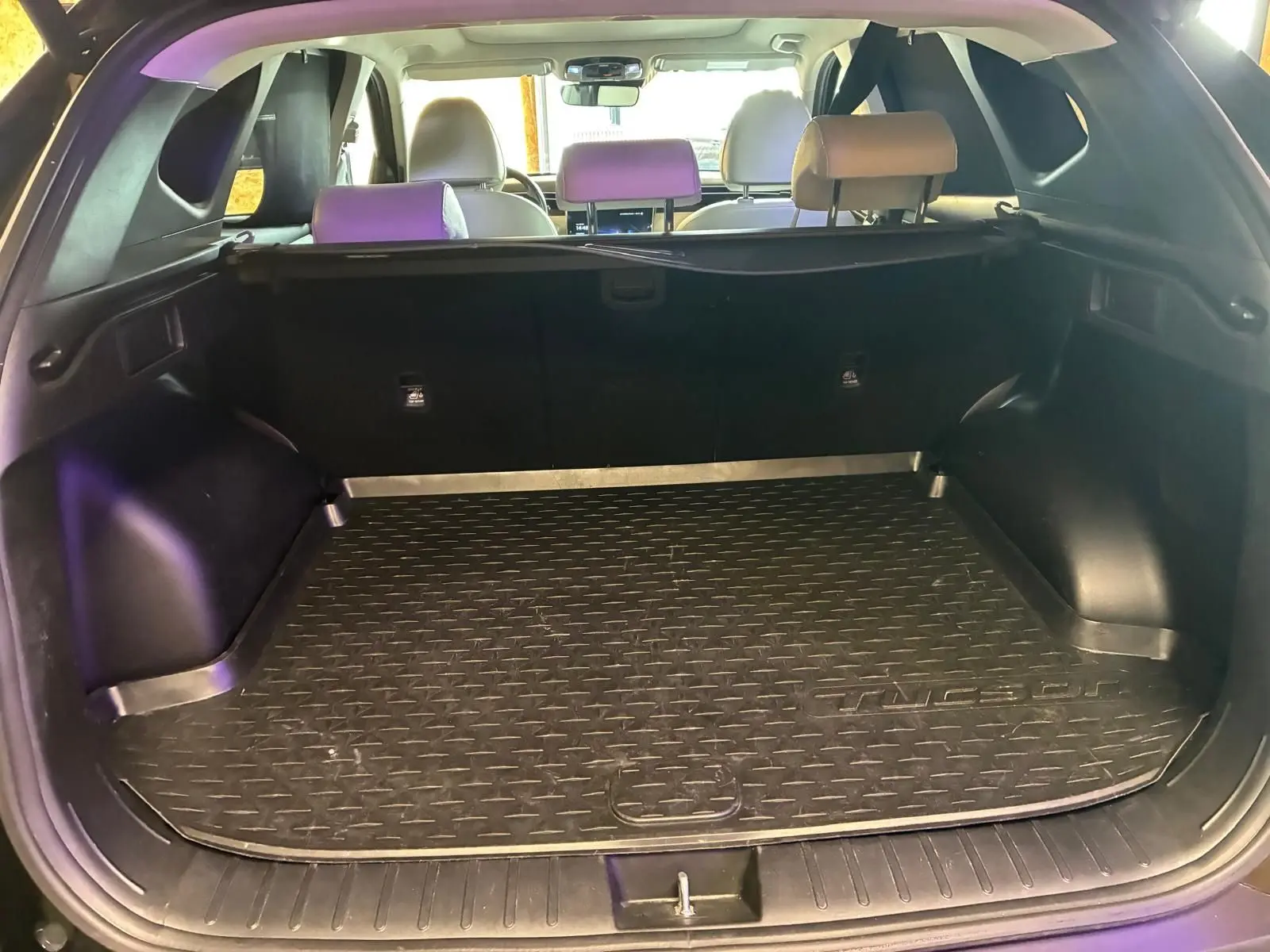 Vue intérieure du coffre ouvert d'un Hyundai Tucson noir 2022, montrant le tapis de coffre et les sièges arrière beiges.