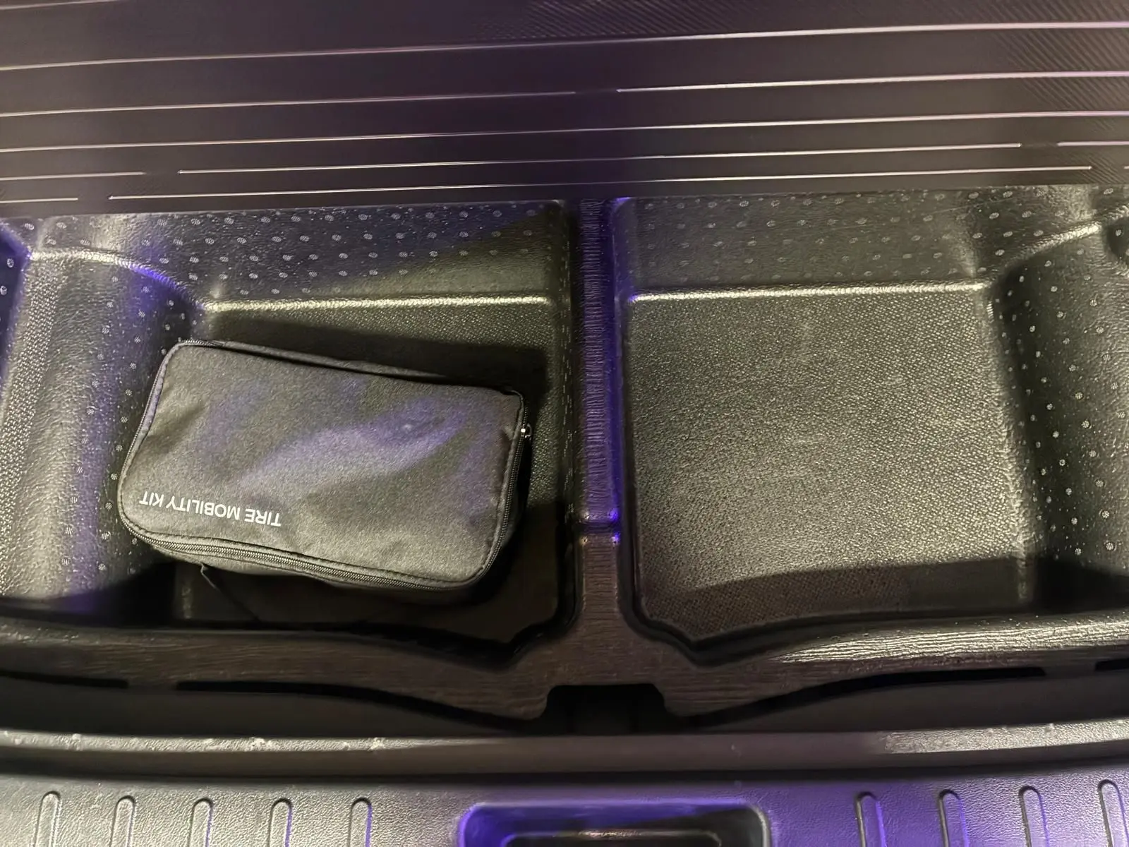 Gros plan sur le rangement sous le coffre du Hyundai Tucson noir 2022, avec trousse de mobilité noire visible.