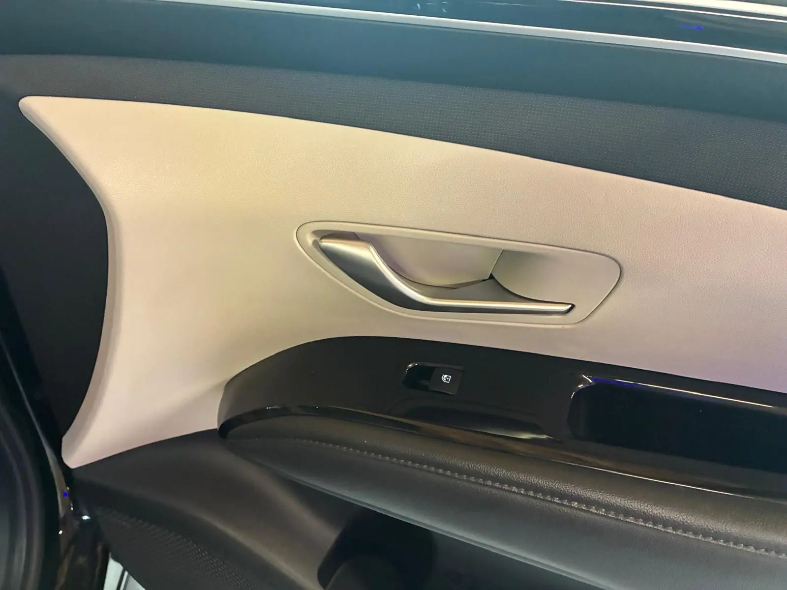 Gros plan sur la poignée intérieure et le panneau de porte beige et noir du Hyundai Tucson 2022 hybride.