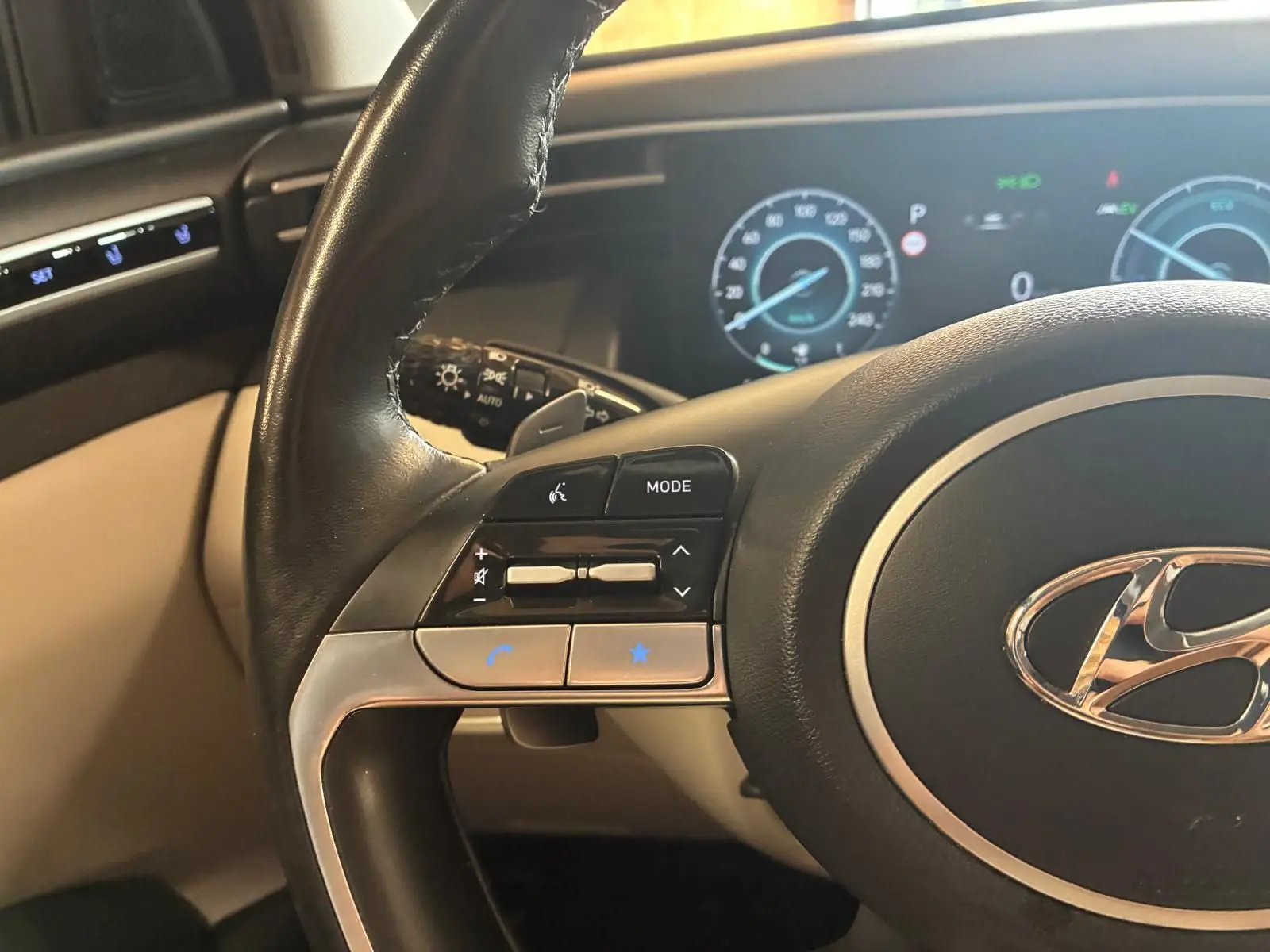 Vue rapprochée du volant noir et beige du Hyundai Tucson 2022, avec commandes intégrées et tableau de bord numérique en arrière-plan.
