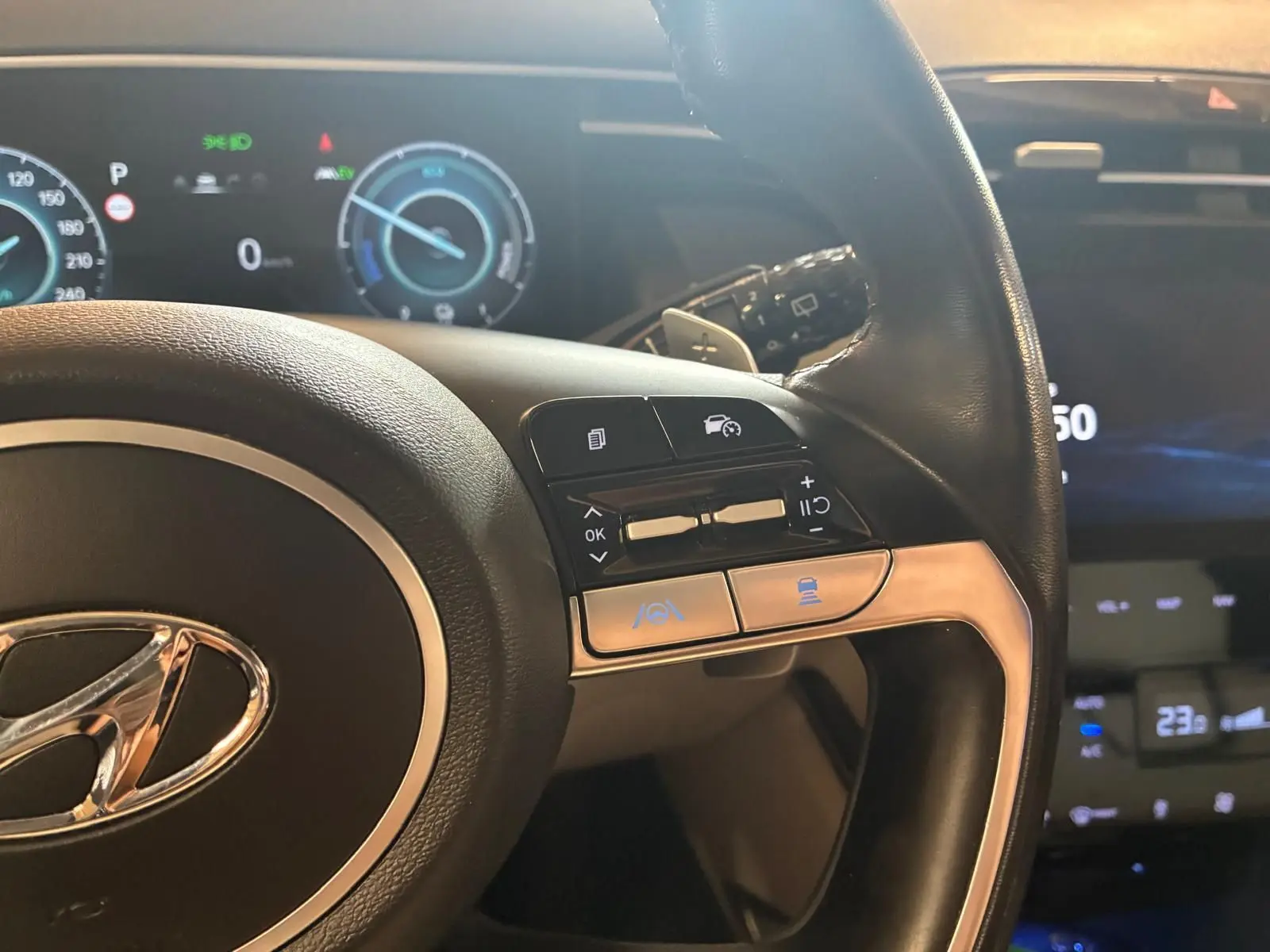 Gros plan sur le volant noir du Hyundai Tucson 2022 avec commandes intégrées et tableau de bord numérique en arrière-plan.