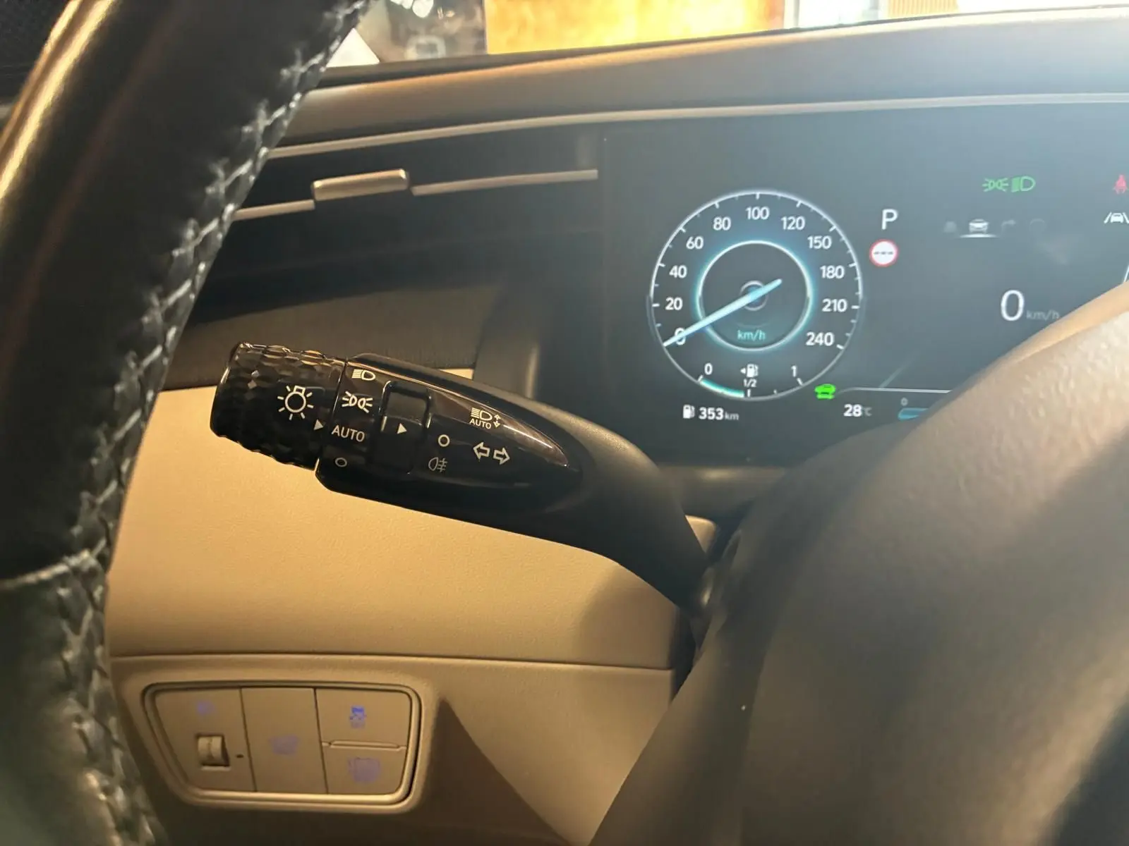 Gros plan sur la manette des phares à gauche du volant dans l’habitacle beige du Hyundai Tucson noir, tableau de bord digital visible.