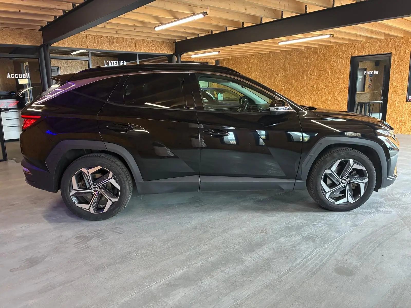 Vue latérale droite d'un Hyundai Tucson noir 2022 hybride avec jantes alliage et lignes anguleuses marquées.