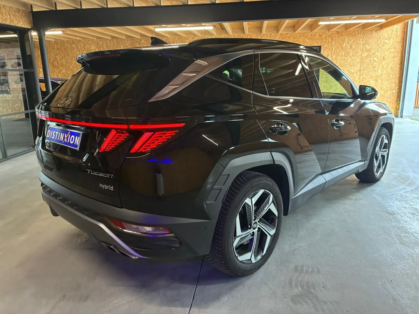 Vue 3/4 arrière droite d'un Hyundai Tucson noir hybride 2022 avec feux arrière LED distinctifs et jantes modernes.