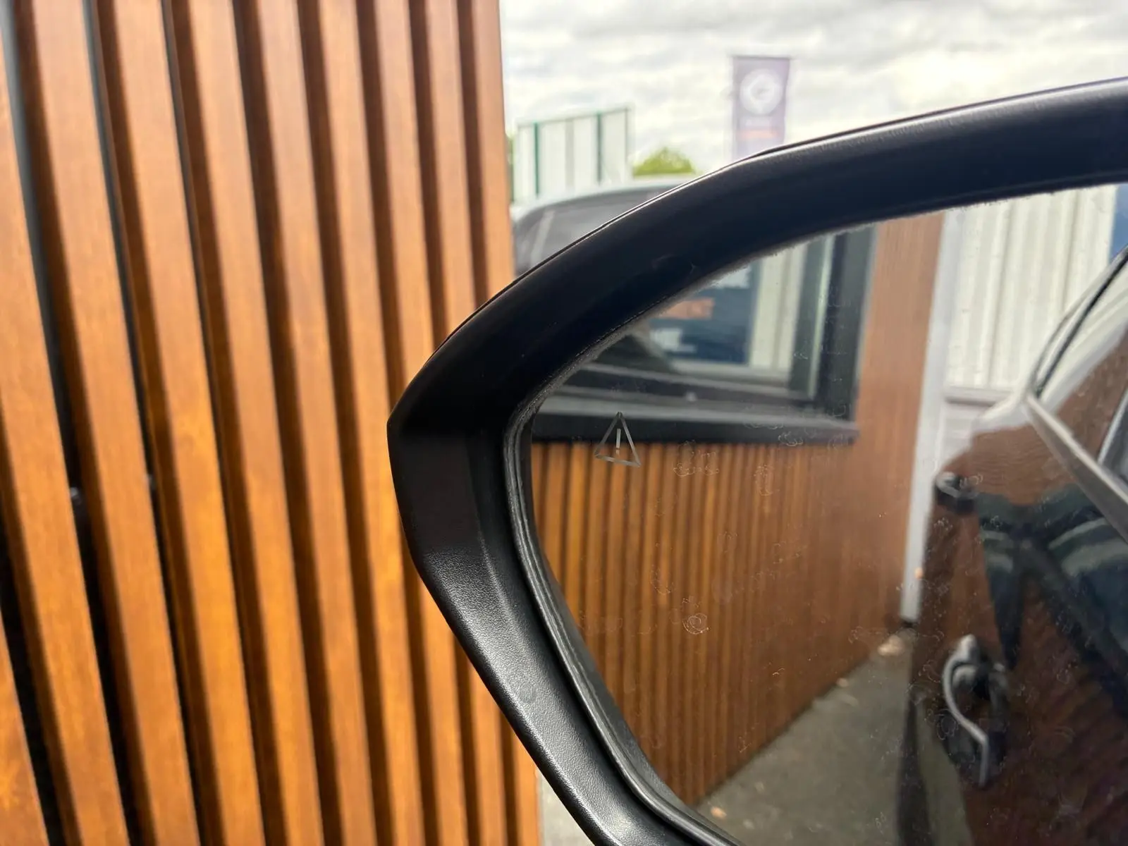 Rétroviseur côté droit du Hyundai Tucson noir 2022, reflétant la carrosserie et un mur en bois vertical.
