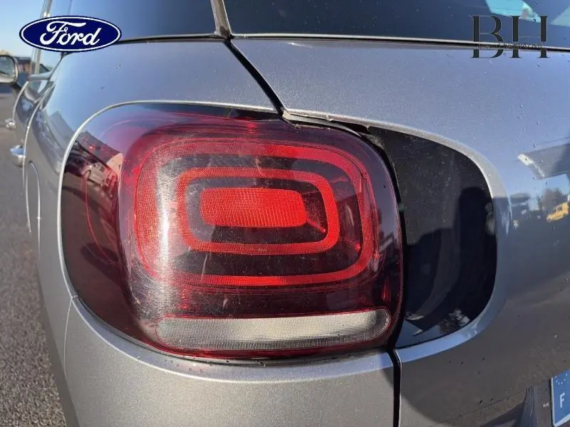 Gros plan sur le feu arrière droit rouge d'une Citroën C3 Aircross gris acier sous lumière naturelle.
