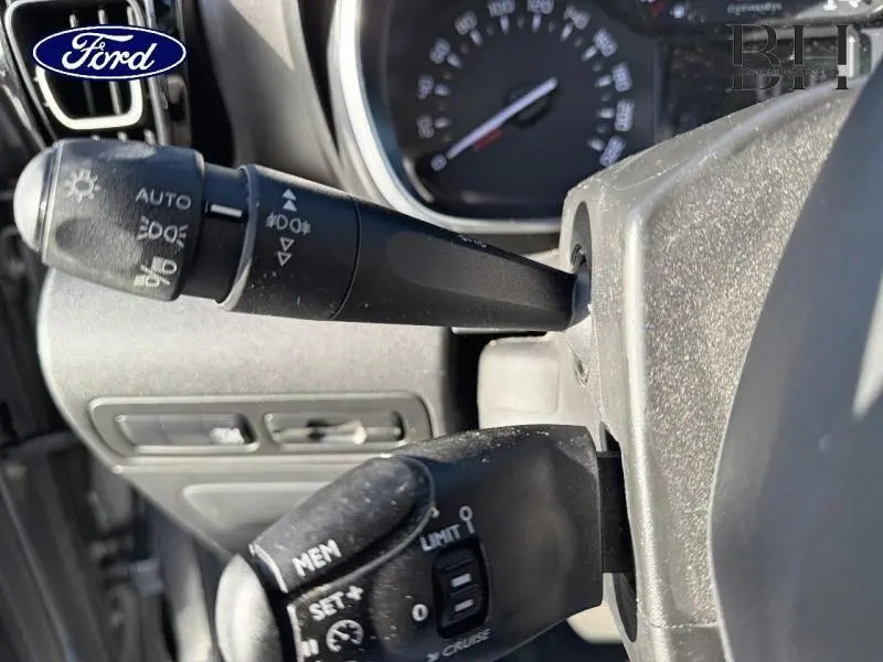 Gros plan sur les commandes au volant côté gauche d'un Citroën C3 Aircross gris acier, avec tableau de bord en arrière-plan.