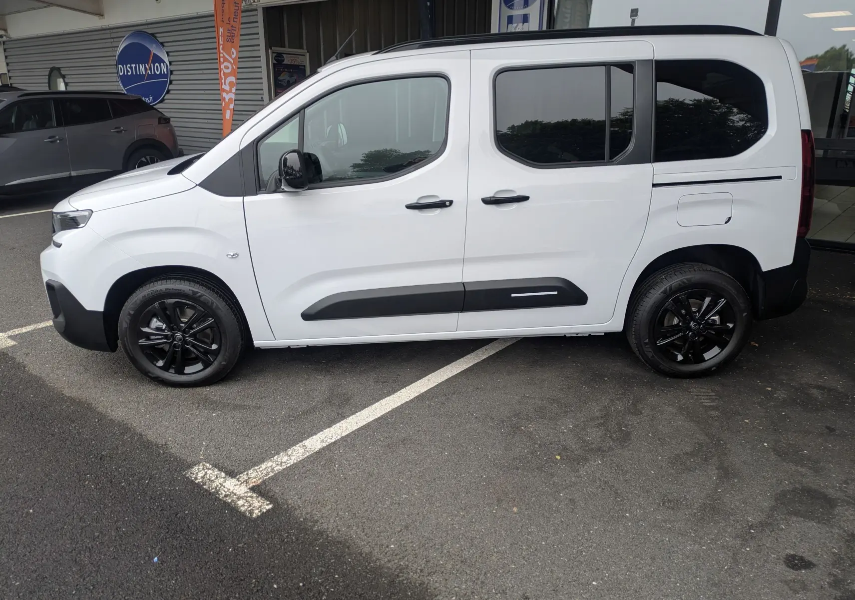 Vue de profil côté gauche d'un Citroën Berlingo blanc 2025 avec jantes noires et protections latérales noires.