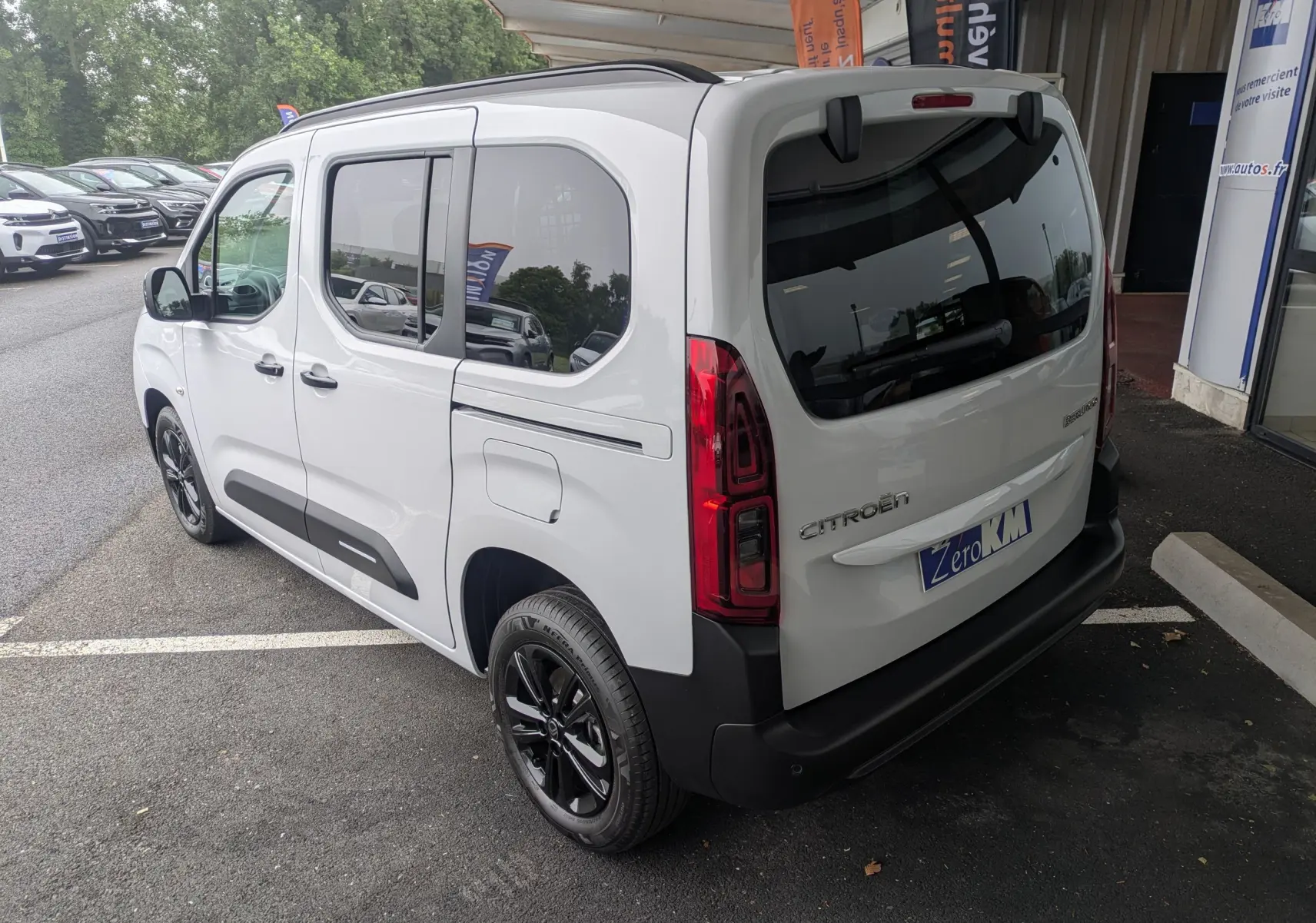 Vue 3/4 arrière droite d'un Citroën Berlingo blanc 2025 avec jantes noires et vitres teintées, stationné en extérieur.
