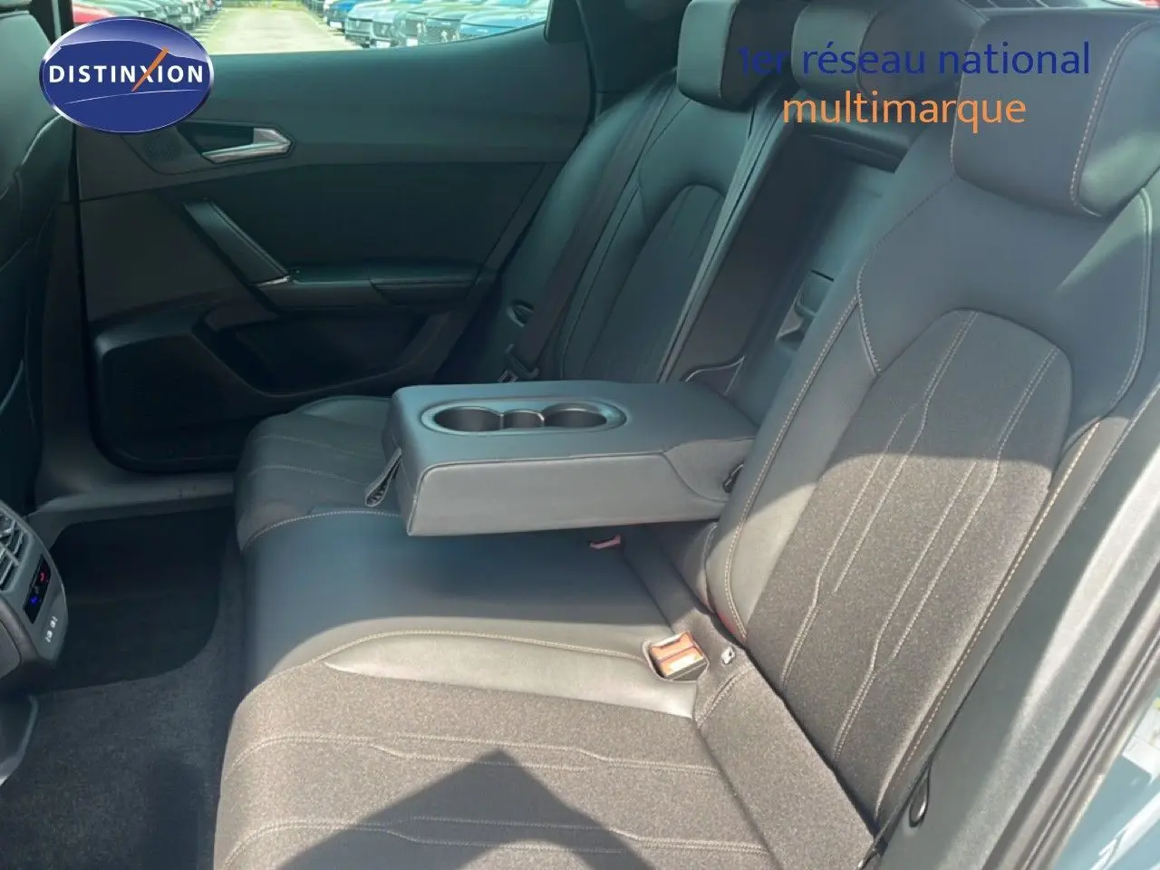Vue intérieure des sièges arrière du CUPRA Formentor 1.5 eTSI en tissu noir avec accoudoir central et porte-gobelets.