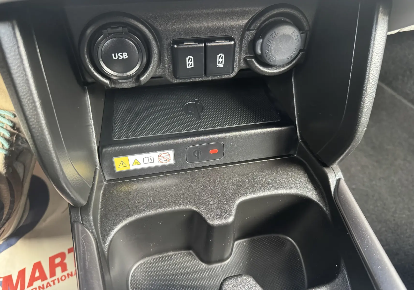 Gros plan sur la console centrale de la Suzuki Swift 1.2 Pack Hybrid 2024, montrant la prise USB, les ports de charge et le chargeur sans fil noir.