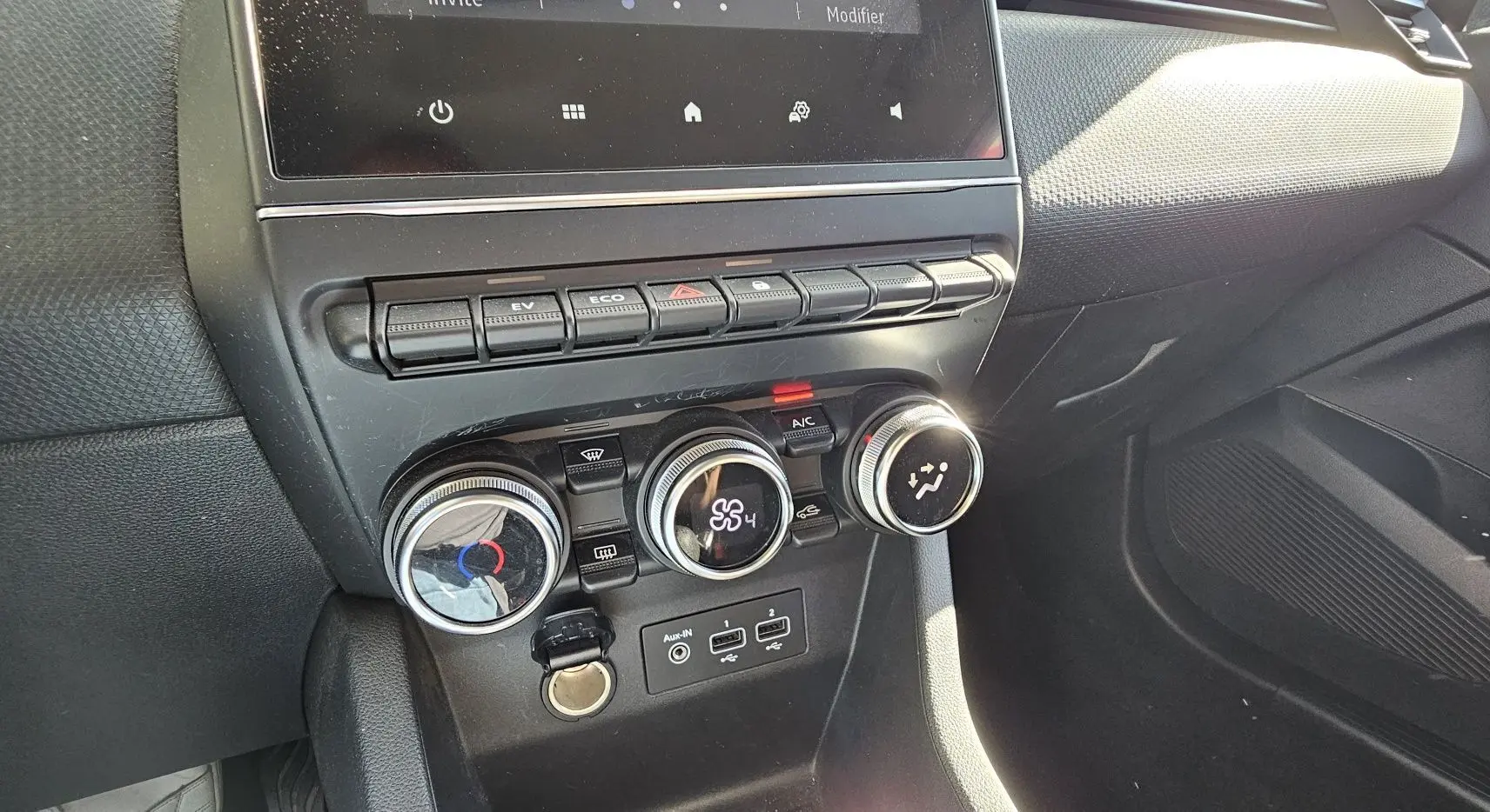 Vue rapprochée de la console centrale de la Renault Clio blanche, mettant en valeur les commandes de climatisation et les boutons de fonction.