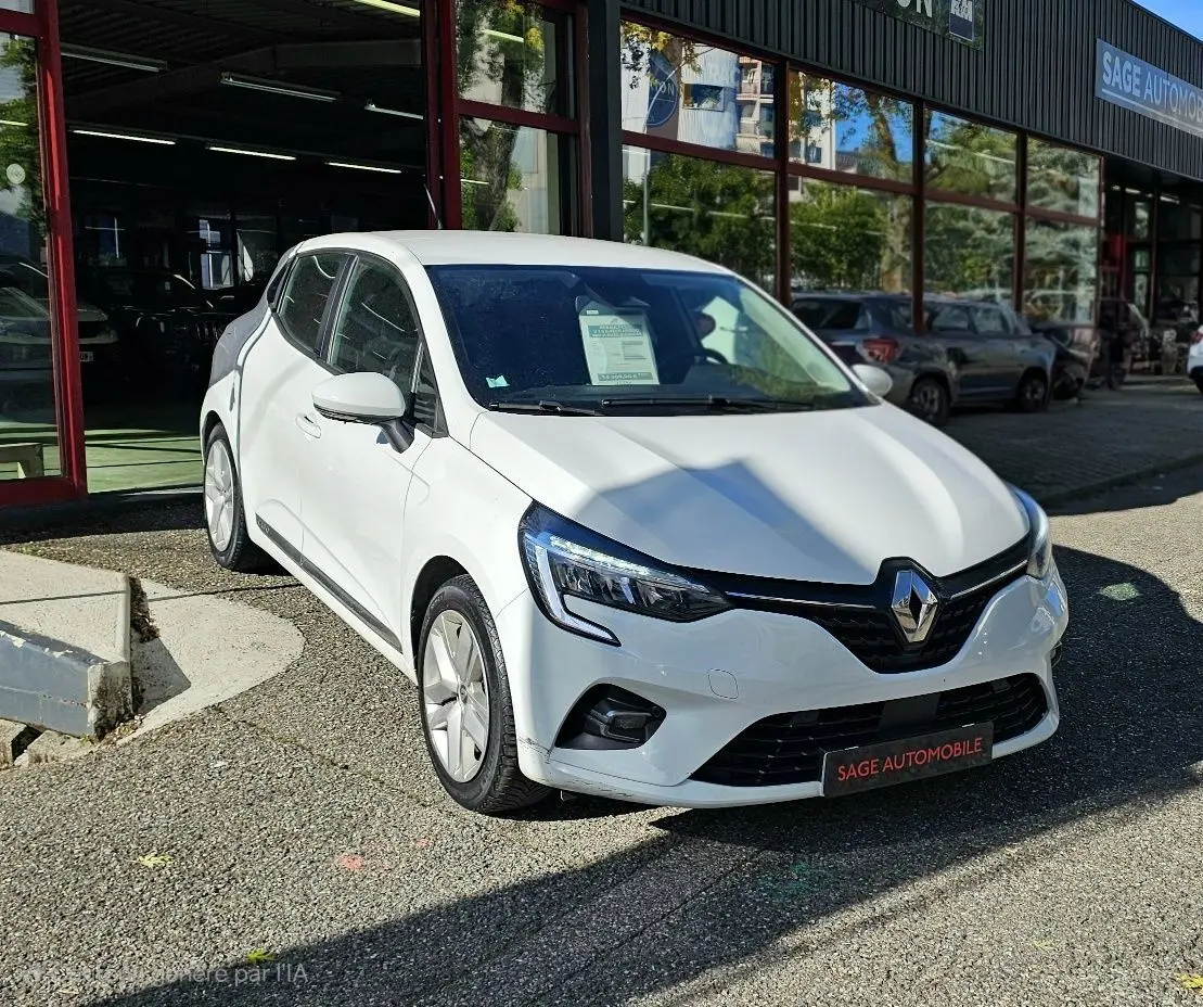 Renault Clio blanche glacier vue 3/4 avant droit, garée devant un showroom avec plaque Sage Automobile.