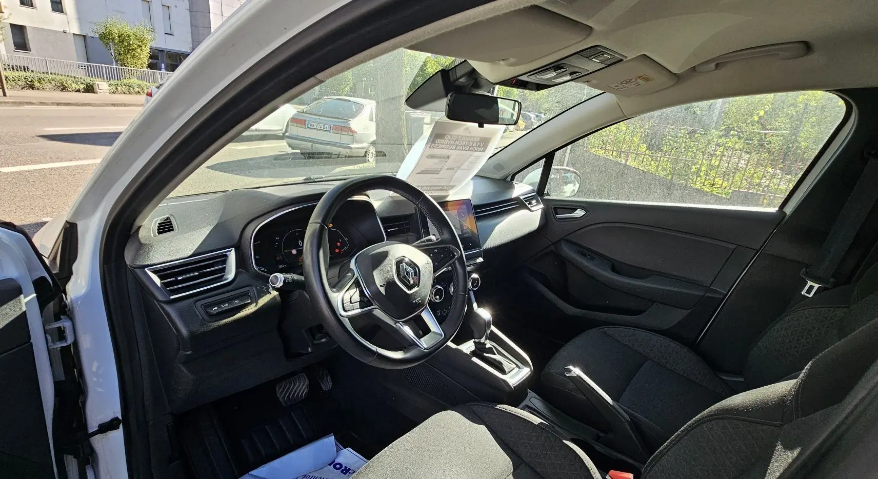 Intérieur de la Renault Clio blanc glacier 2021, vue côté conducteur, tableau de bord moderne avec écran tactile et volant multifonction.