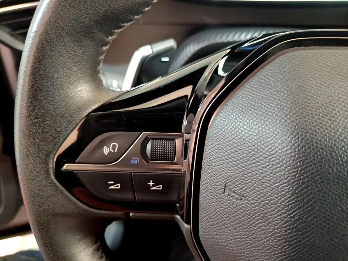 Gros plan sur les commandes vocales et volume du volant cuir noir du Peugeot 2008 gris clair 2021 PureTech.