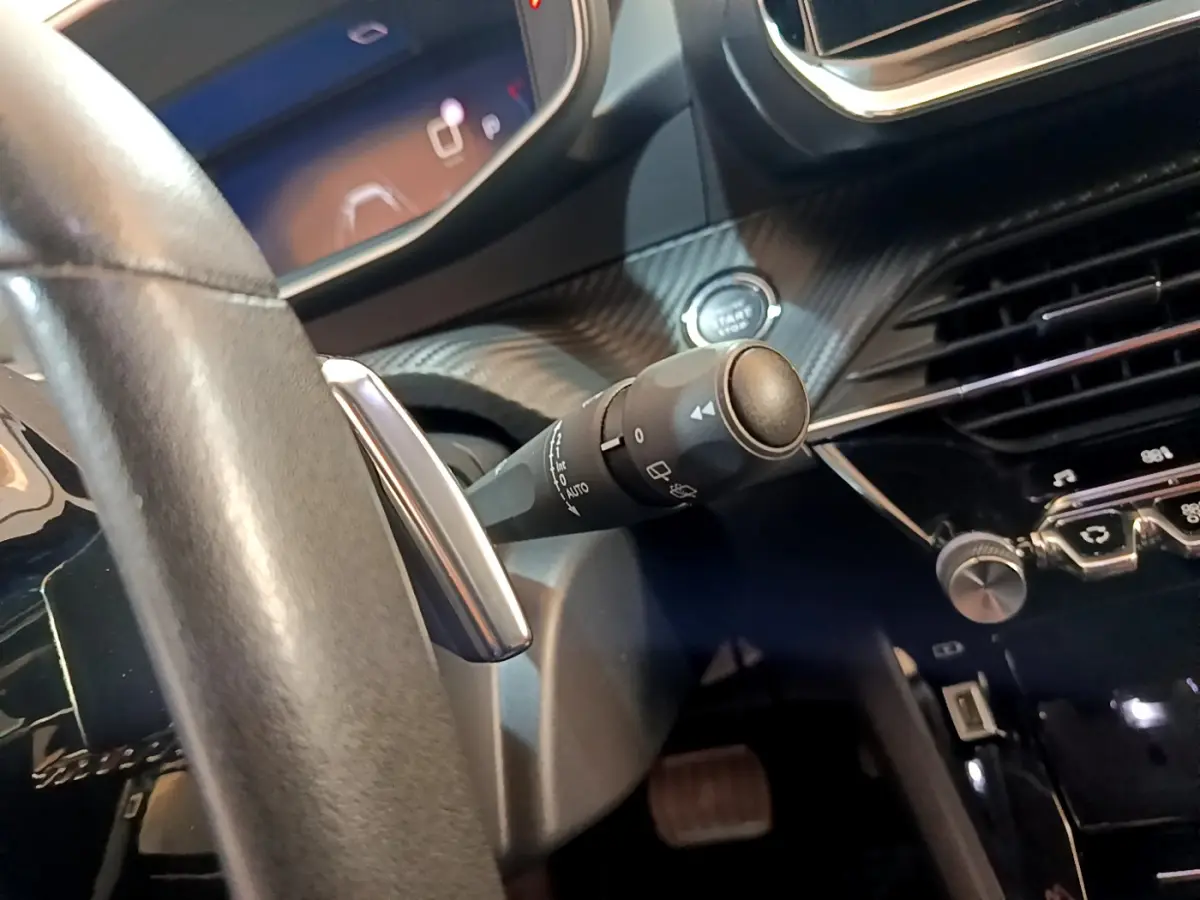Gros plan sur la commande d’essuie-glace à gauche du volant cuir du Peugeot 2008 gris clair, tableau de bord moderne.