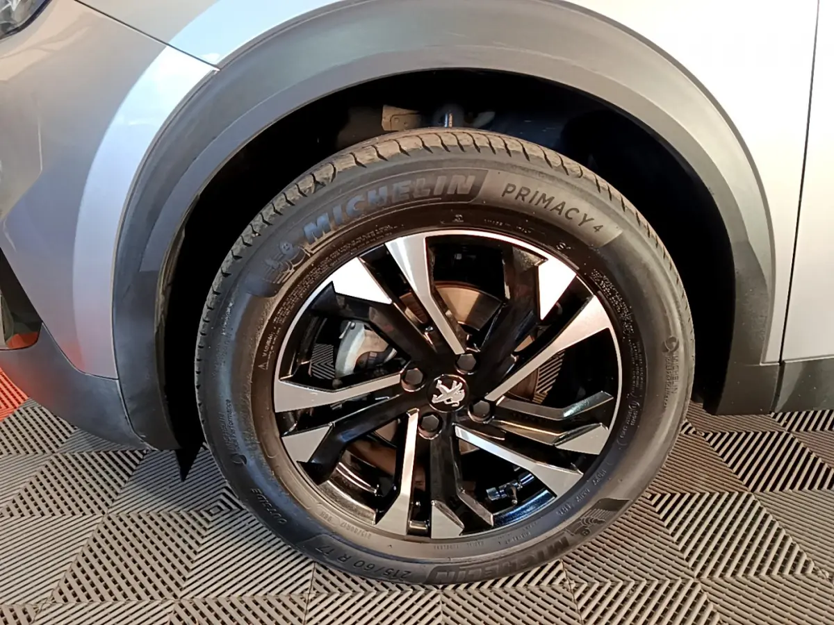 Gros plan sur la roue avant gauche d’un Peugeot 2008 gris clair avec jante alliage noire et argentée.