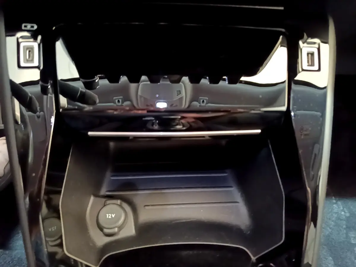 Prise 12V et rangement noir sous la console centrale du Peugeot 2008 gris clair, vue intérieure rapprochée.