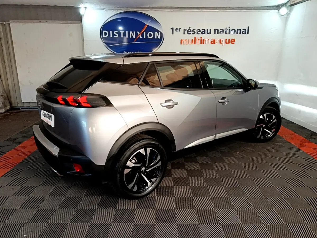 Peugeot 2008 gris clair vue 3/4 arrière droit, avec feux arrière LED et jantes noires stylisées.