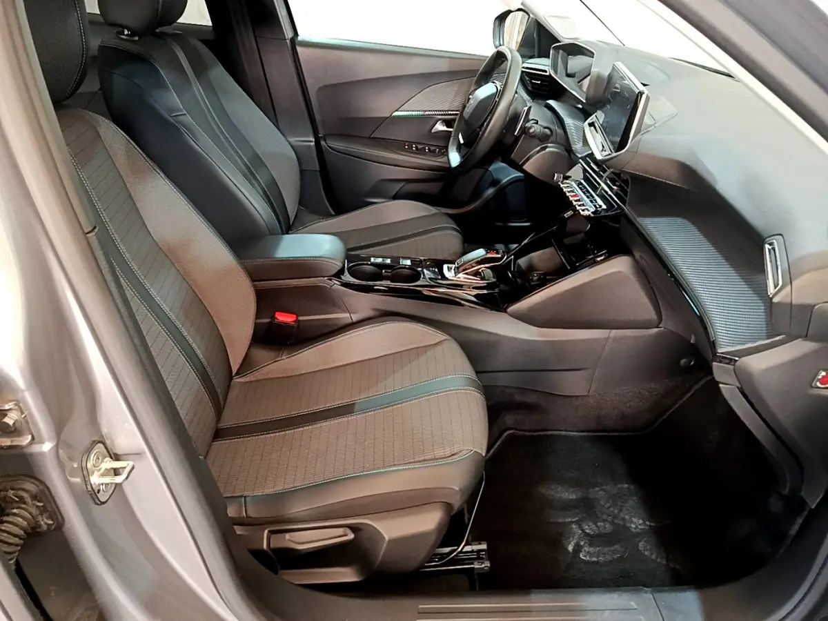 Intérieur avant droit du Peugeot 2008 gris clair 2021, sièges tissu, tableau de bord avec écran tactile et volant cuir.