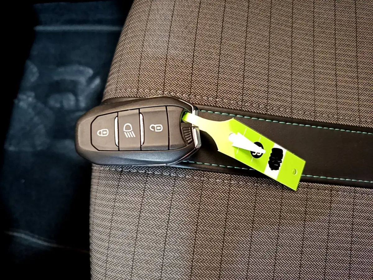 Clé de voiture Peugeot 2008 PureTech posée sur un siège tissu gris clair avec surpiqûres bleues.