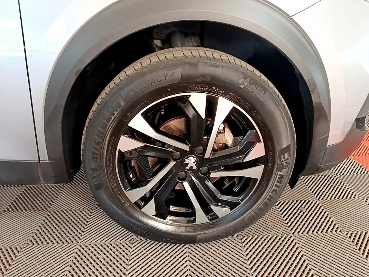 Gros plan sur la roue avant gauche du Peugeot 2008 gris clair, jante alliage noire et argentée au design moderne.