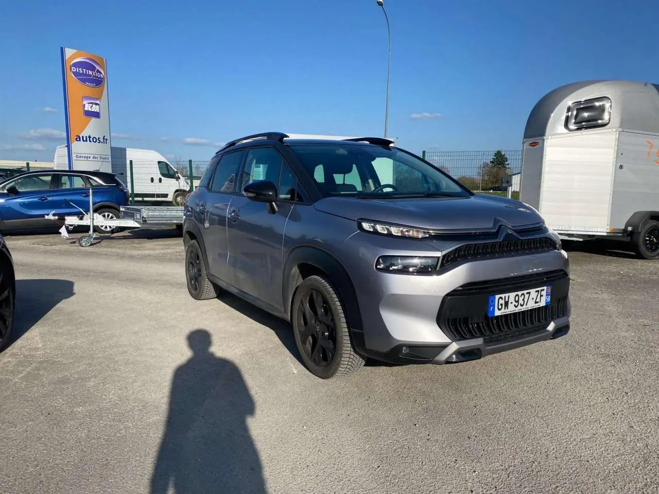 Vue 3/4 avant droit d'un Citroën C3 Aircross 2024 gris foncé avec jantes noires, stationné en extérieur au soleil.