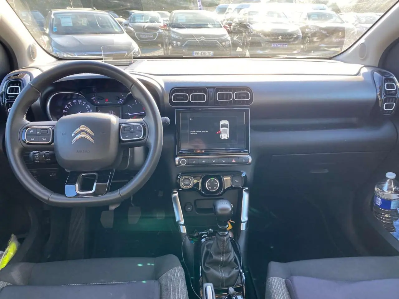 Vue intérieure frontale du tableau de bord et volant noir du Citroën C3 Aircross gris foncé 2024 avec écran tactile et boîte manuelle.