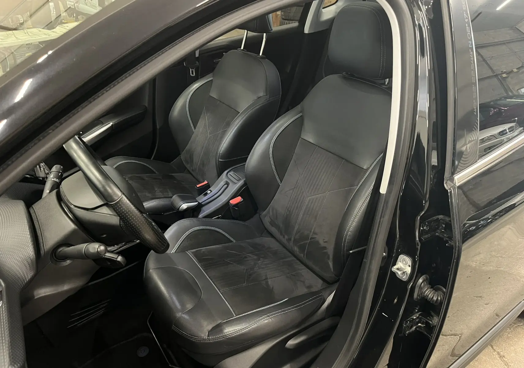 Vue intérieure côté conducteur du Peugeot 2008 noir de 2018, mettant en valeur les sièges en cuir noir et le volant.