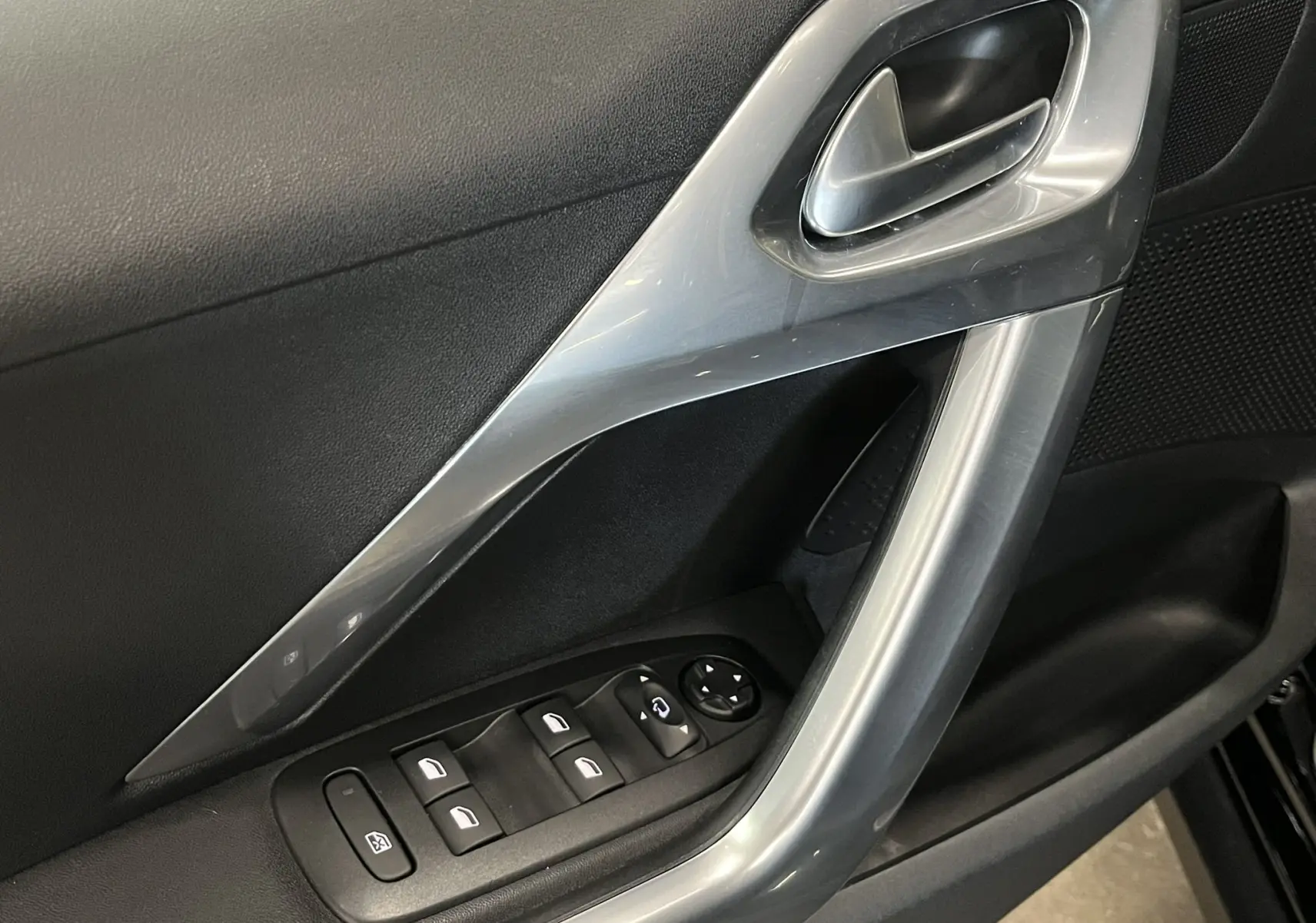 Gros plan sur la poignée intérieure et les commandes de vitres côté gauche d’une Peugeot 2008 noire de 2018.
