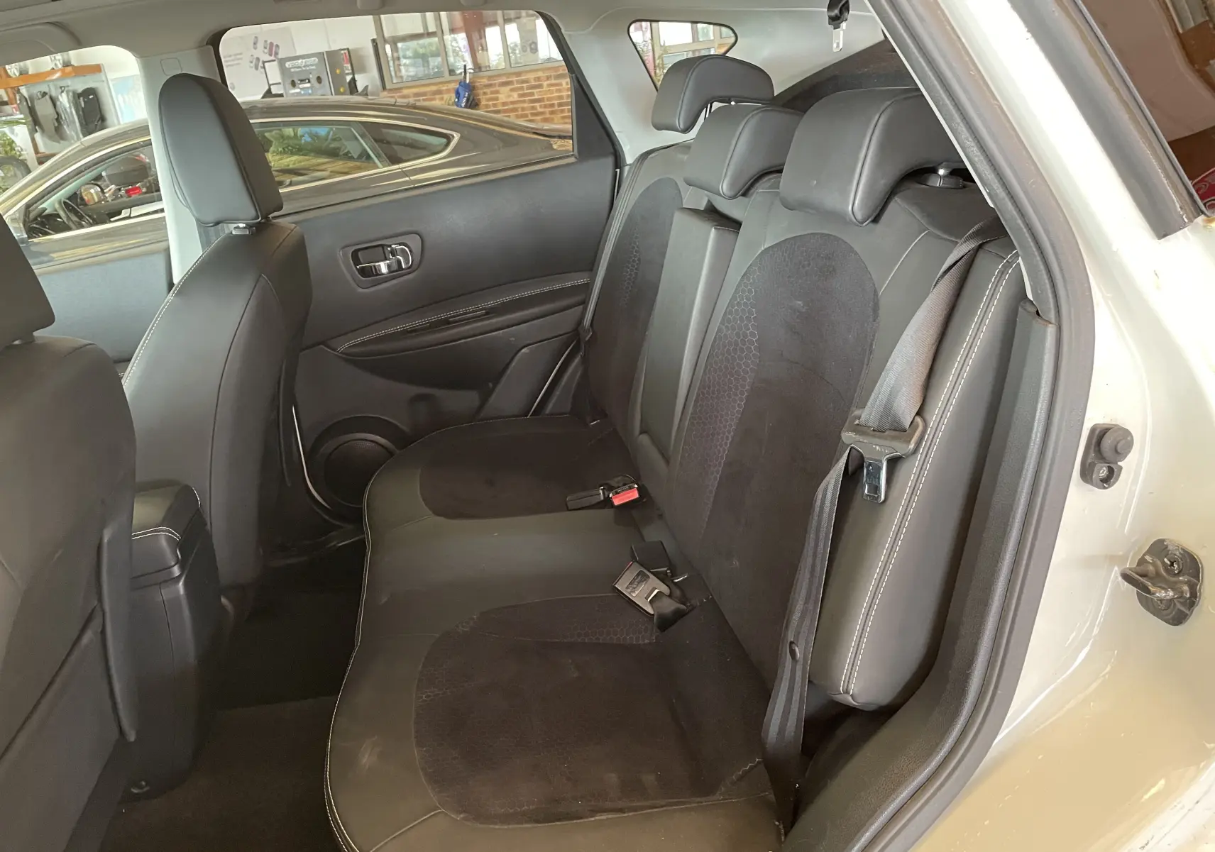 Vue intérieure côté droit des sièges arrière noirs en tissu et cuir du Nissan Qashqai blanc 2013 avec porte ouverte.